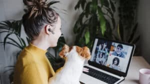 image of 2 colleagues in meeting room on virtual call with other team members about leadership in a hybrid work environment and leading a hybrid workforce